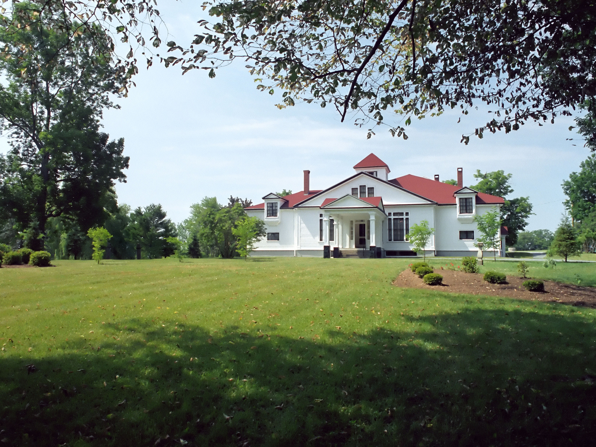 Exterior view of Clifton Museum Park, formerly Haliburton House Museum, a white two-story building with a red roof, surrounded by a large green lawn and trees under a sunny sky.